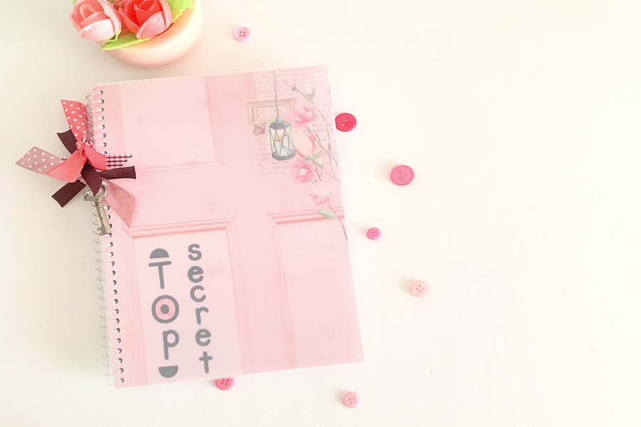 el cuaderno alterado estilo scrapbooking en color rosa y con dos lazos en el espiral a modo de decoracion 