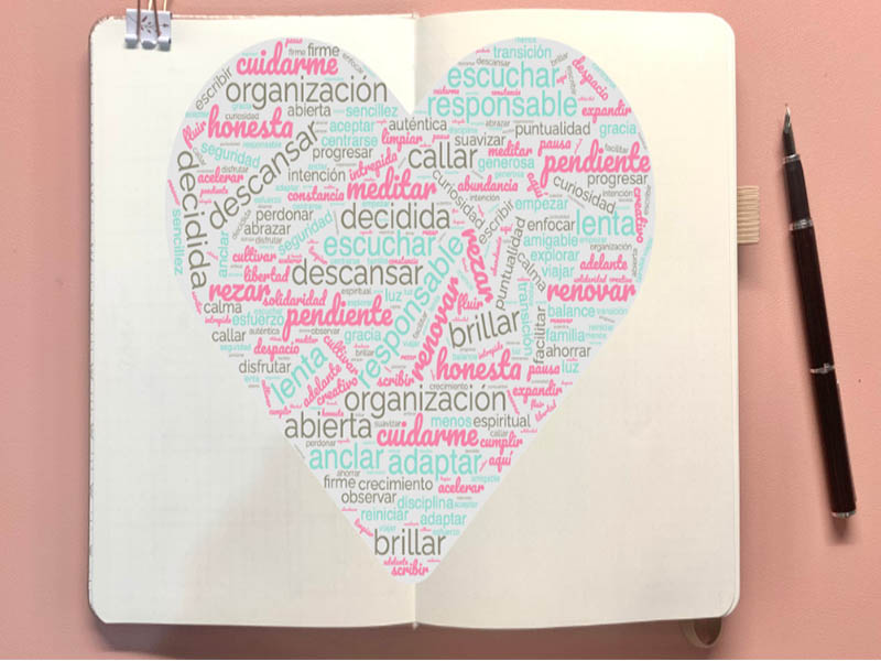 un cuaderno abierto y al centro hay palabras en color rosa y verde menta que forman un corazon.
